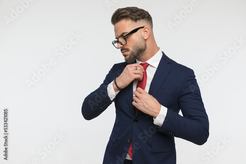 sexy stylish businessman with beard looking to side and adjusting tie