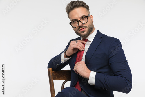 arrogant young businessman sitting on chair and adjusting red tie photo