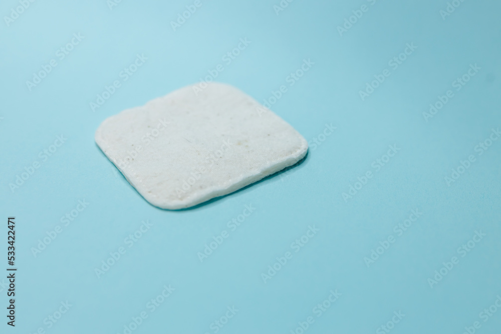 White cotton square made of bamboo and cotton wool on a light blue background. Cotton swab for cosmetology, make-up and hygiene White cotton square made of bamboo and cotton wool on a light blue background. Cotton swab for cosmetology, make-up and hygiene