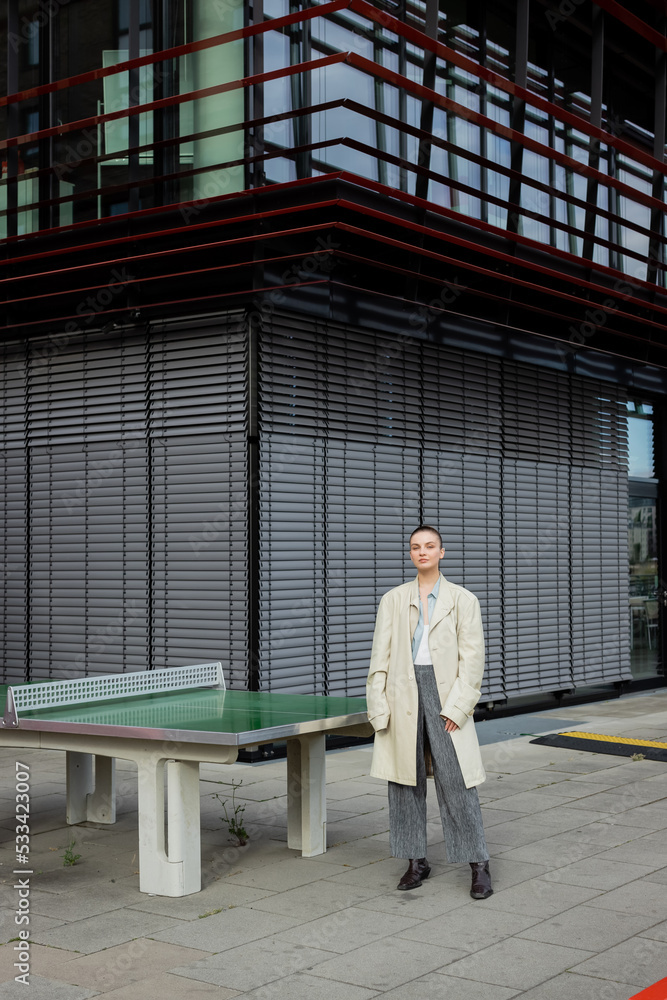 Stylish woman in trench coat standing near ping-pong table outdoors in Berlin. Stylish woman in trench coat standing near ping-pong table outdoors in Berlin.