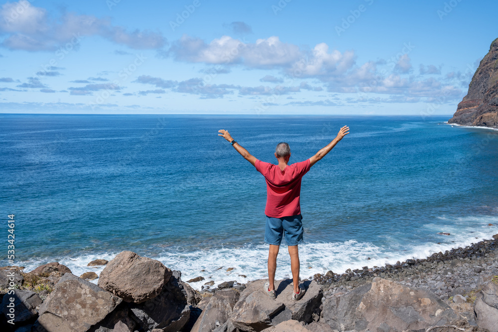Man with open arms embracing nature on a beautiful island, back view