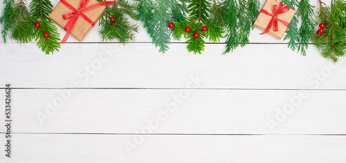 Christmas background with fir tree branches red decorations and gift boxes on white wood banner.