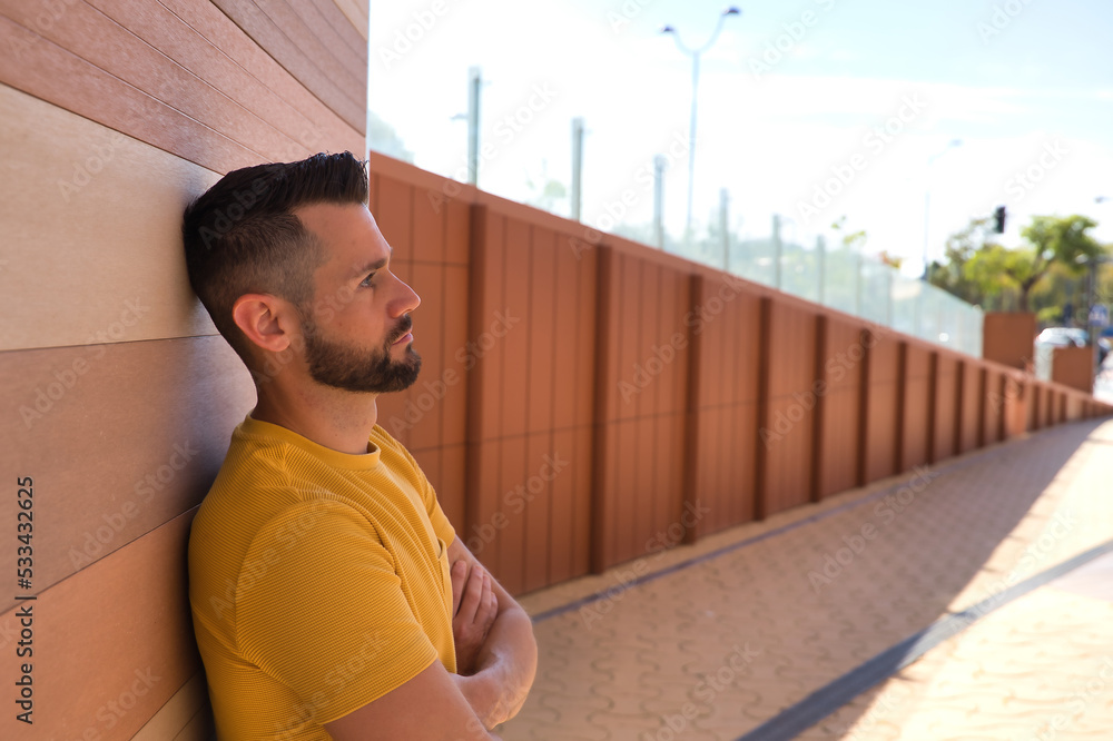 Fototapeta premium Portrait of handsome young man, with blue eyes and yellow shirt, with his arms crossed and his head leaning against a wall very worried. Concept beauty, fashion, problems, worry, trend.