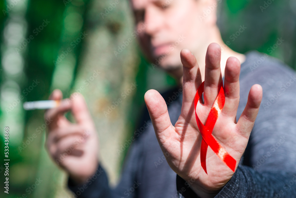 Smoking Man holding red aids ribbon in hand at summer day.World aids day concept.