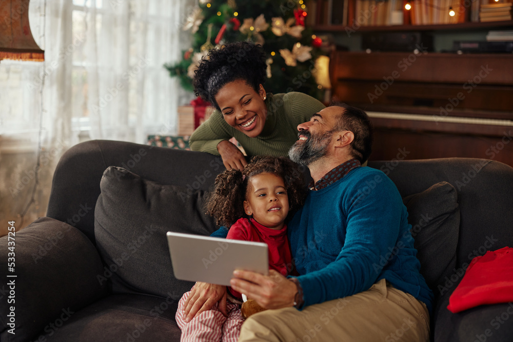 Cheerful parents and daughter celebrating Christmas with family via digital tablet