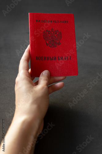 Young woman holding in her hand Military ID citizen of the Russian Federation, the concept of mobilization in Russia. Translation: Russian Federation, Military ID photo