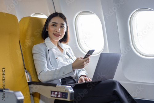Traveling and technology. Flying at first class. Pretty young Asian business woman using smartphone while sitting in airplane.