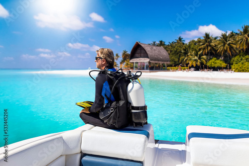 A scuba diver in his diving gear sits in front of a boat and enjoys the view of the tropical landscape with turquoise sea