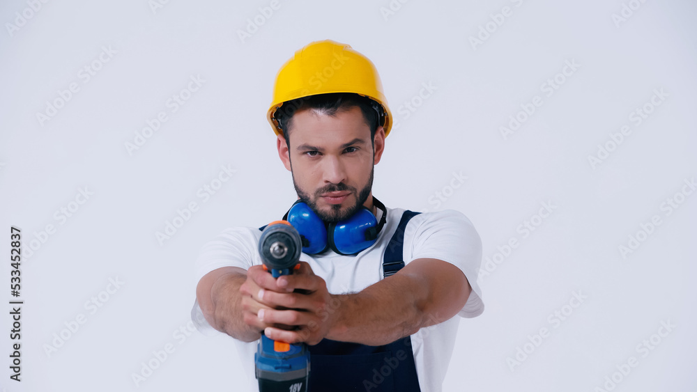 repairman in hardhat holding electric drill and looking at camera isolated on white. repairman in hardhat holding electric drill and looking at camera isolated on white.