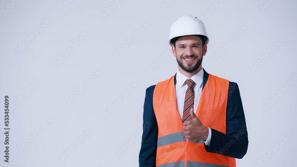 happy foreman in safety vest and helmet showing thumb up isolated on grey. happy foreman in safety vest and helmet showing thumb up isolated on grey.