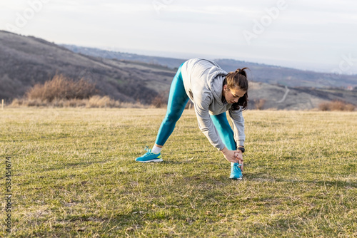Young woman stretching before jogging in the middle of the field so far away from urban city in fresh air