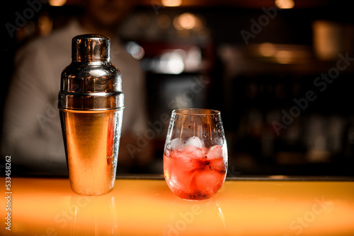 close-up view of shaker and glass of cocktail on yellow table