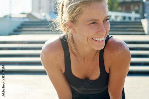 Young cheerful blond sportswoman in black activewear enjoying break after outdoor sports training while standing in front of camera