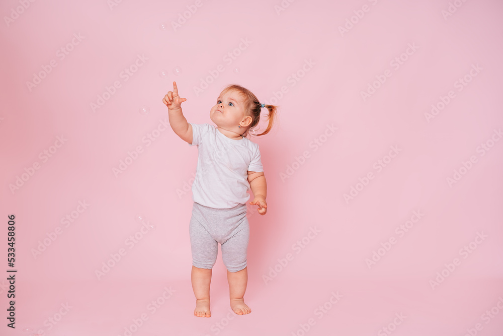Cute little happy girl standing, looking and pointing up on a pink background, Advertising of children's goods Cute little happy girl standing, looking and pointing up on a pink background, Advertising of children's goods