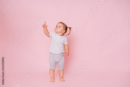Cute little happy girl standing, looking and pointing up on a pink background, Advertising of children's goods