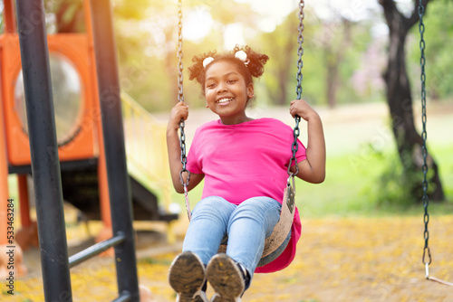 Smiling African American child girl playing on swing at the playground. Happy girl having fun on swing outdoor