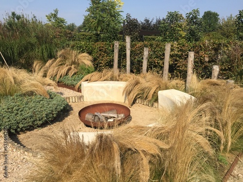 Beach patio with a fire pit and a cozy seating area under a canopy. Summer garden with swaying grasses, shell paths and fire place of Corten steel  photo