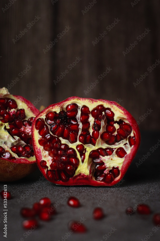 close up of a cut pomegranate on grey table and wooden dark background
