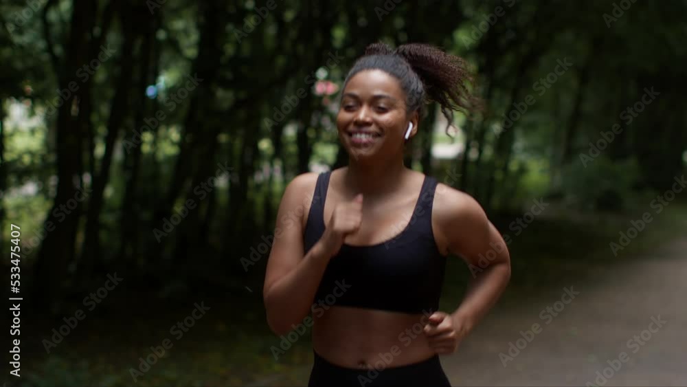 Young sporty african american lady athlete enjoying morning run workout in public park, listening to music via earbuds Young sporty african american lady athlete enjoying morning run workout in public park, listening to music via earbuds