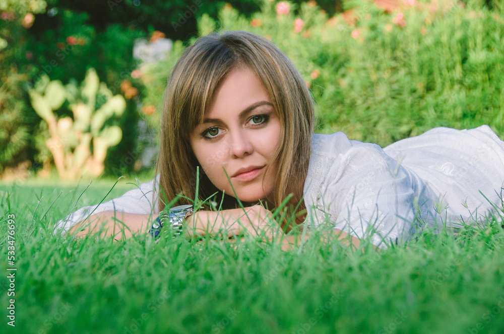 A young beautiful woman relaxing on a green lawn on a bright sunny day. A woman in a public park for recreation in a tropical climate. A young beautiful woman relaxing on a green lawn on a bright sunny day. A woman in a public park for recreation in a tropical climate.