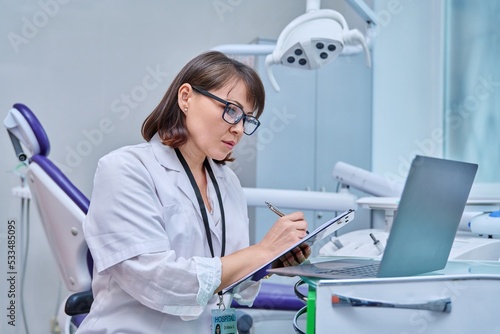 Принти на полотні Doctor dentist working in office, using laptop, making notes on clipboard