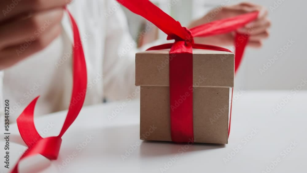 Closeup female hands untie gift red ribbon bow falling box open, holiday gift in woman hands