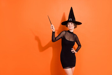 Photo of lovely young lady wave magic stick wear stylish halloween witch black hermione granger costume isolated on orange background