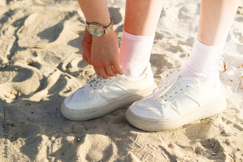 Legs of a girl in a skirt in fashionable sneakers on the sand  the image is taken for a walk.