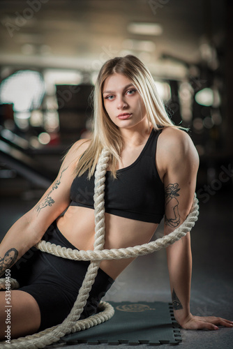 Portrait of a young beautiful blonde girl with a rope in the gym.