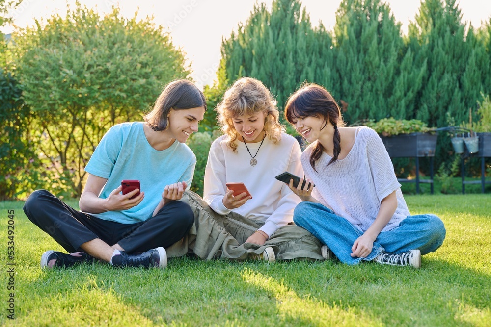 Teenage friends sitting on the grass with smartphones Teenage friends sitting on the grass with smartphones