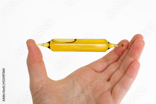 A hand holds an ampoule with liquid contents. Glass medicine vial mockup design. Medical dietary supplements. Vitamin complex. Person holds a medicinal product close-up. Cosmetics elixir. Copy space