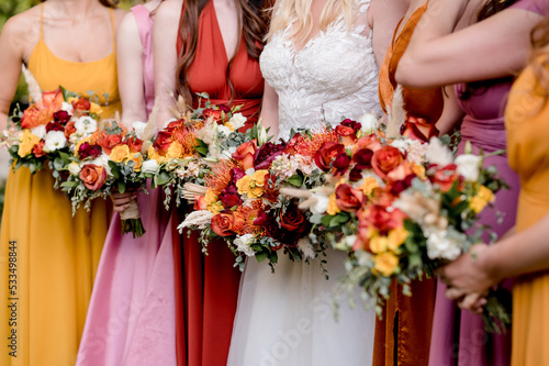 Bride and Bridesmaids in autumn colors holding colorful bouquets filled with orange roses and yellow anemones, close up crop no faces