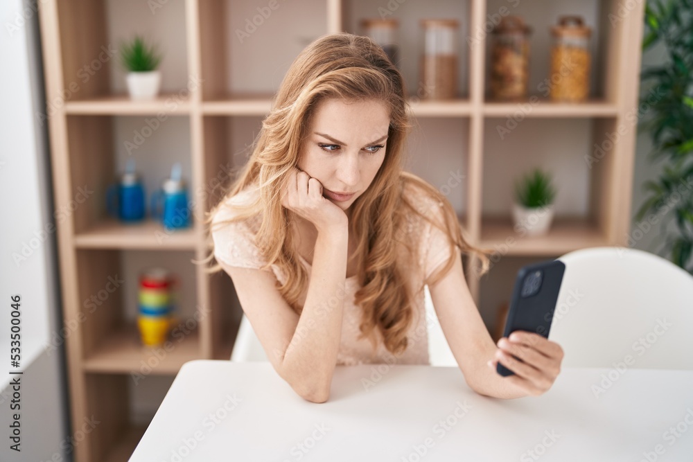 Young blonde woman using smartphone with serious expression at home Young blonde woman using smartphone with serious expression at home