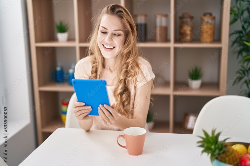 Young blonde woman using touchpad drinking coffee at home Young blonde woman using touchpad drinking coffee at home
