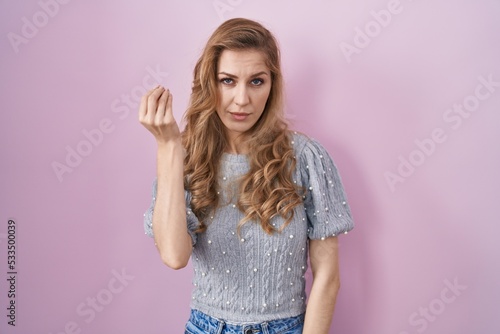 Beautiful blonde woman standing over pink background doing italian gesture with hand and fingers confident expression © Krakenimages.com