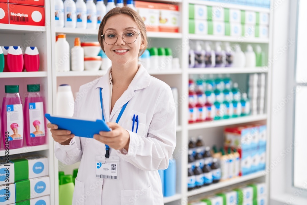 Young blonde woman pharmacist using touchpad working at pharmacy