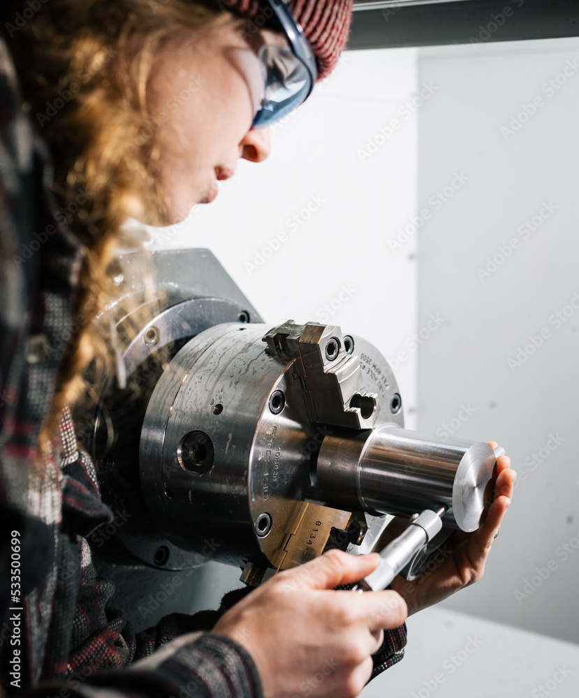 Industrial woman machinist uses a CNC lathe machine and a micrometer Industrial woman machinist uses a CNC lathe machine and a micrometer