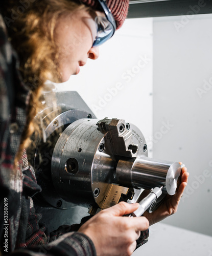 Industrial woman machinist uses a CNC lathe machine and a micrometer for calibration