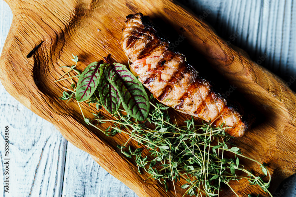 Grilled salmon fish fillet with green salad on the wooden cutting board, close up. Delicious food in the restaurant menu. Concept of catering service Grilled salmon fish fillet with green salad on the wooden cutting board, close up. Delicious food in the restaurant menu. Concept of catering service