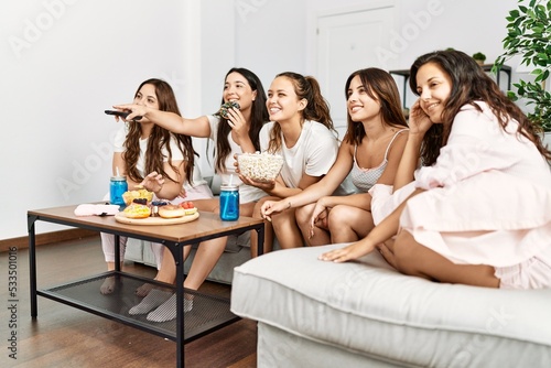 Group of young hispanic women celebrating pajamas party watching movie at home.