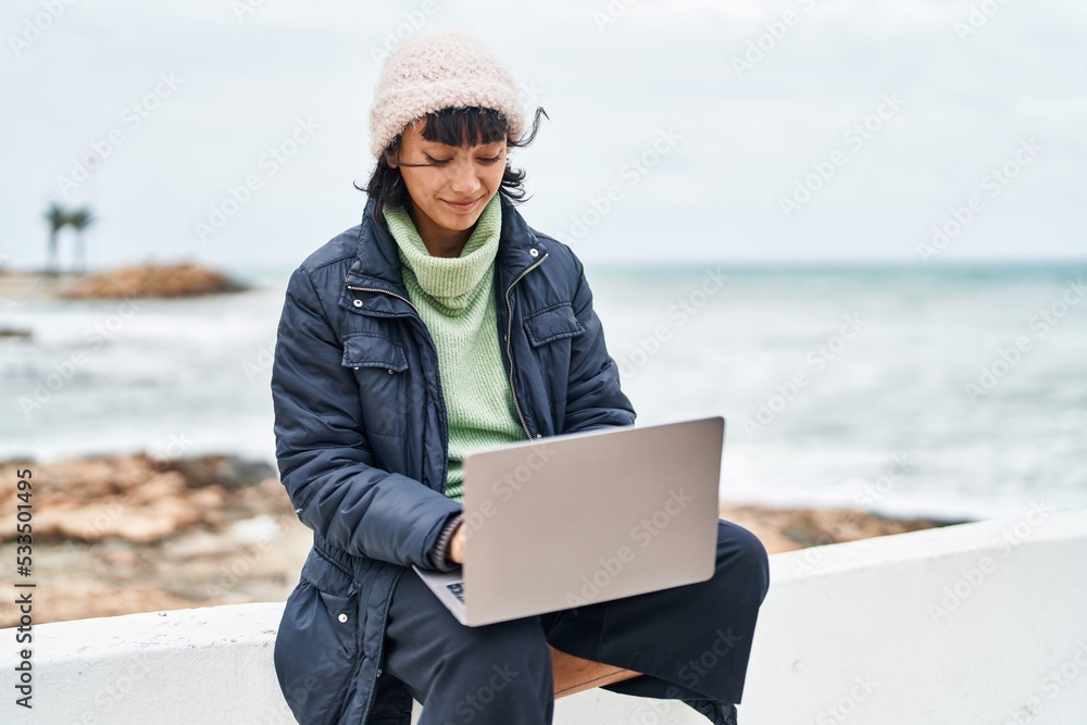 Young beautiful hispanic woman smiling confident using laptop at seaside