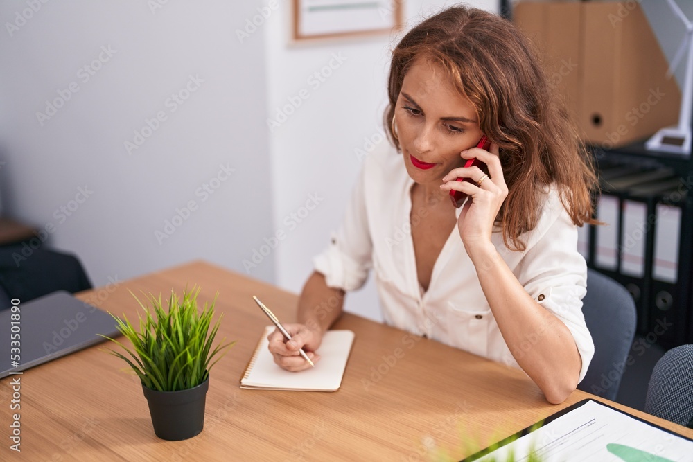 Young beautiful hispanic woman business worker talking on smartphone writing on notebook at office Young beautiful hispanic woman business worker talking on smartphone writing on notebook at office