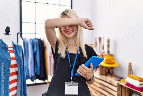 Young blonde woman working as manager at retail boutique smiling cheerful playing peek a boo with hands showing face. surprised and exited
