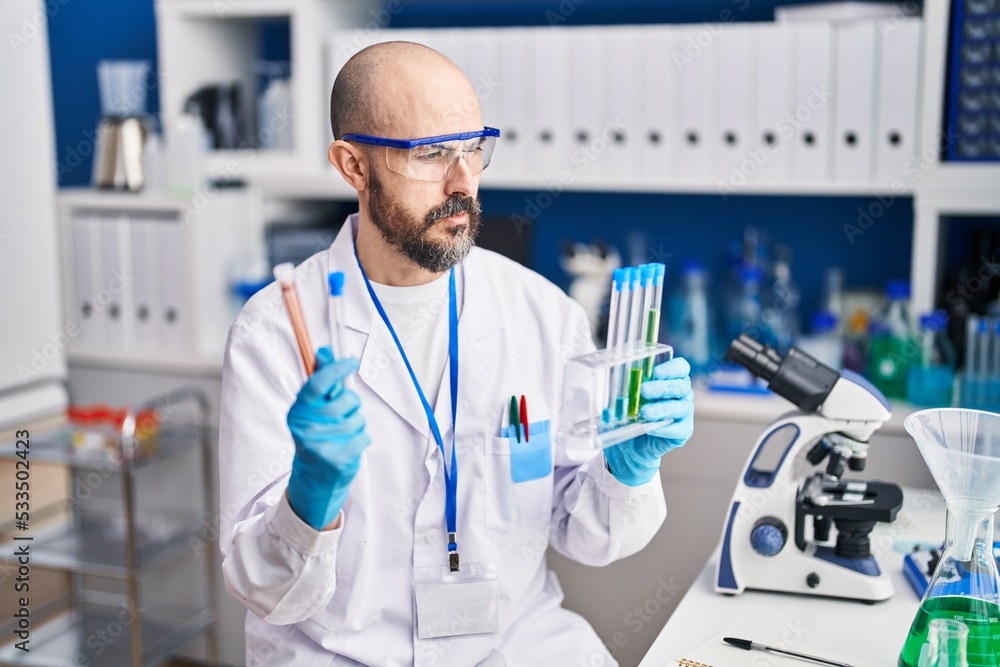 Young bald man scientist holding test tubes at laboratory