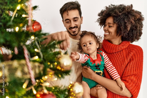Couple and daughter smiling confident decorating christmas tree at home