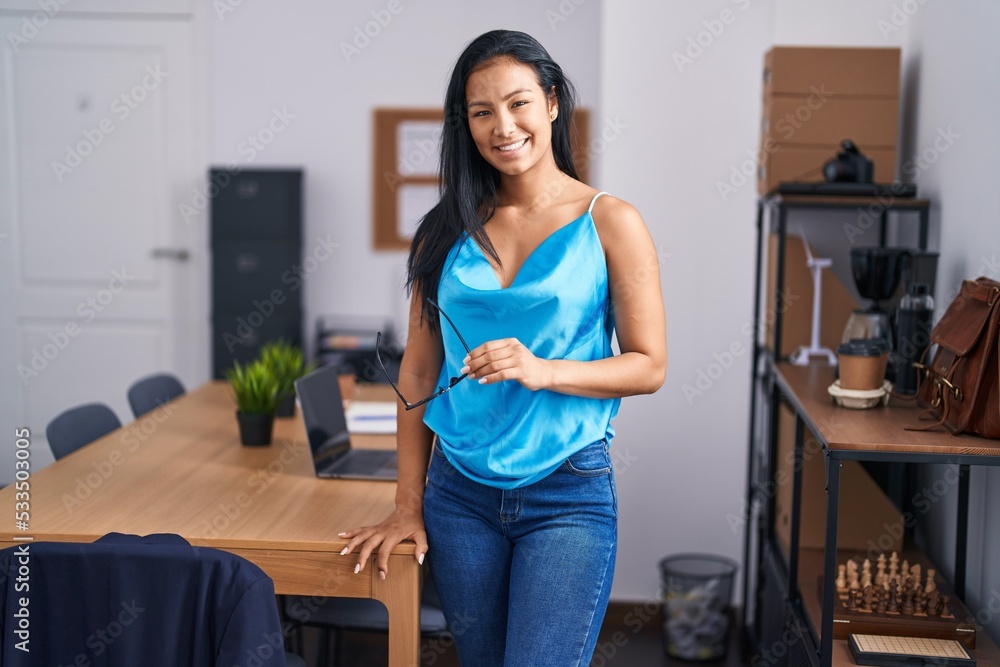 Young beautiful latin woman business worker smiling confident holding glasses at office