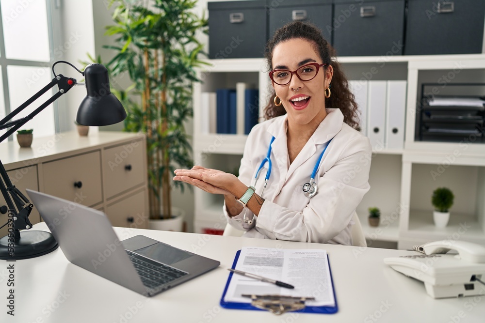 Young hispanic woman wearing doctor uniform and stethoscope pointing aside with hands open palms showing copy space, presenting advertisement smiling excited happy Young hispanic woman wearing doctor uniform and stethoscope pointing aside with hands open palms showing copy space, presenting advertisement smiling excited happy