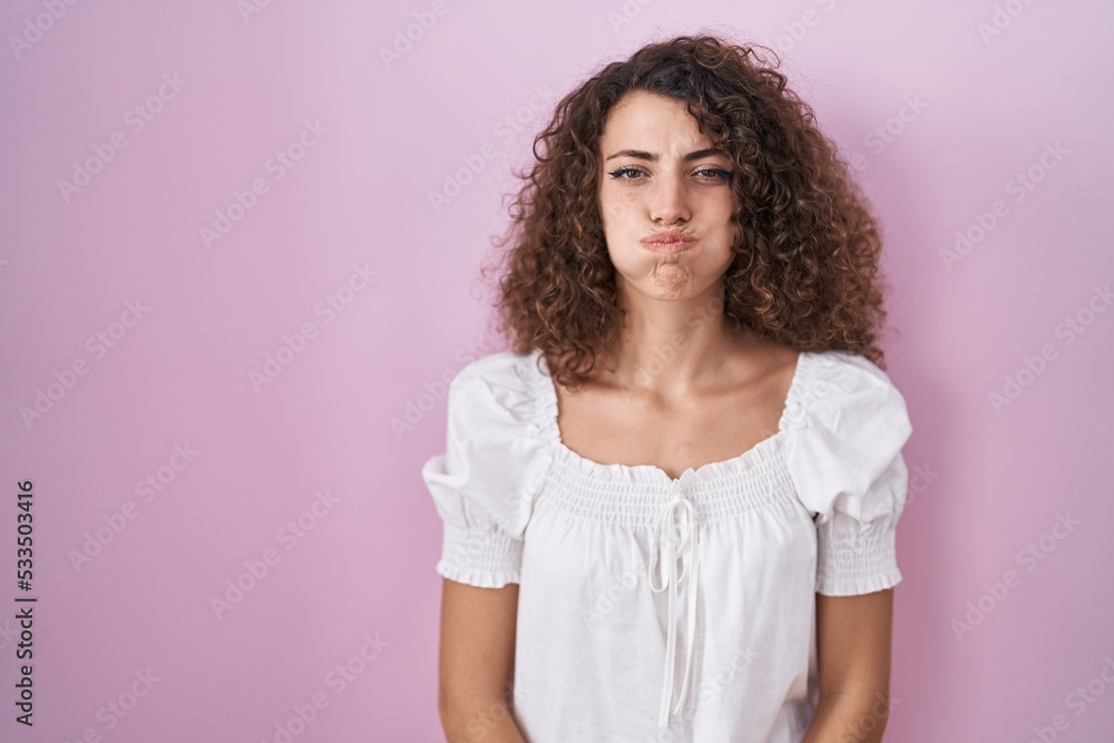 Hispanic woman with curly hair standing over pink background puffing cheeks with funny face. mouth inflated with air, crazy expression. Hispanic woman with curly hair standing over pink background puffing cheeks with funny face. mouth inflated with air, crazy expression.