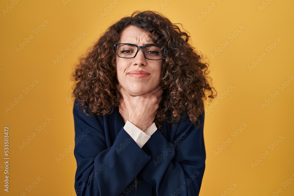 Hispanic woman with curly hair standing over yellow background shouting and suffocate because painful strangle. health problem. asphyxiate and suicide concept.