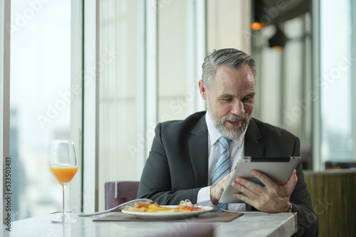 Caucasian Businessman using tablet computer. Happy middle aged man sitting in a restaurant. Entrepreneur working online  reading finance report  thinking.